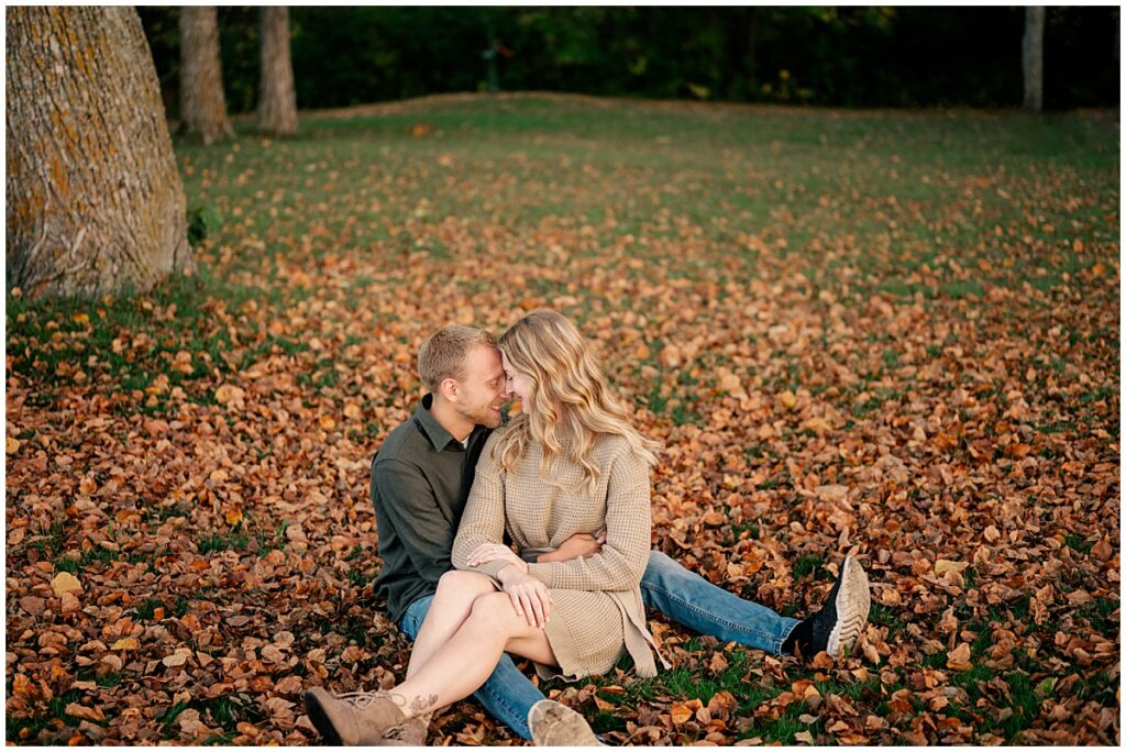 woman sits in man's lap among fallen leaves during Fall Engagement at Mississippi River