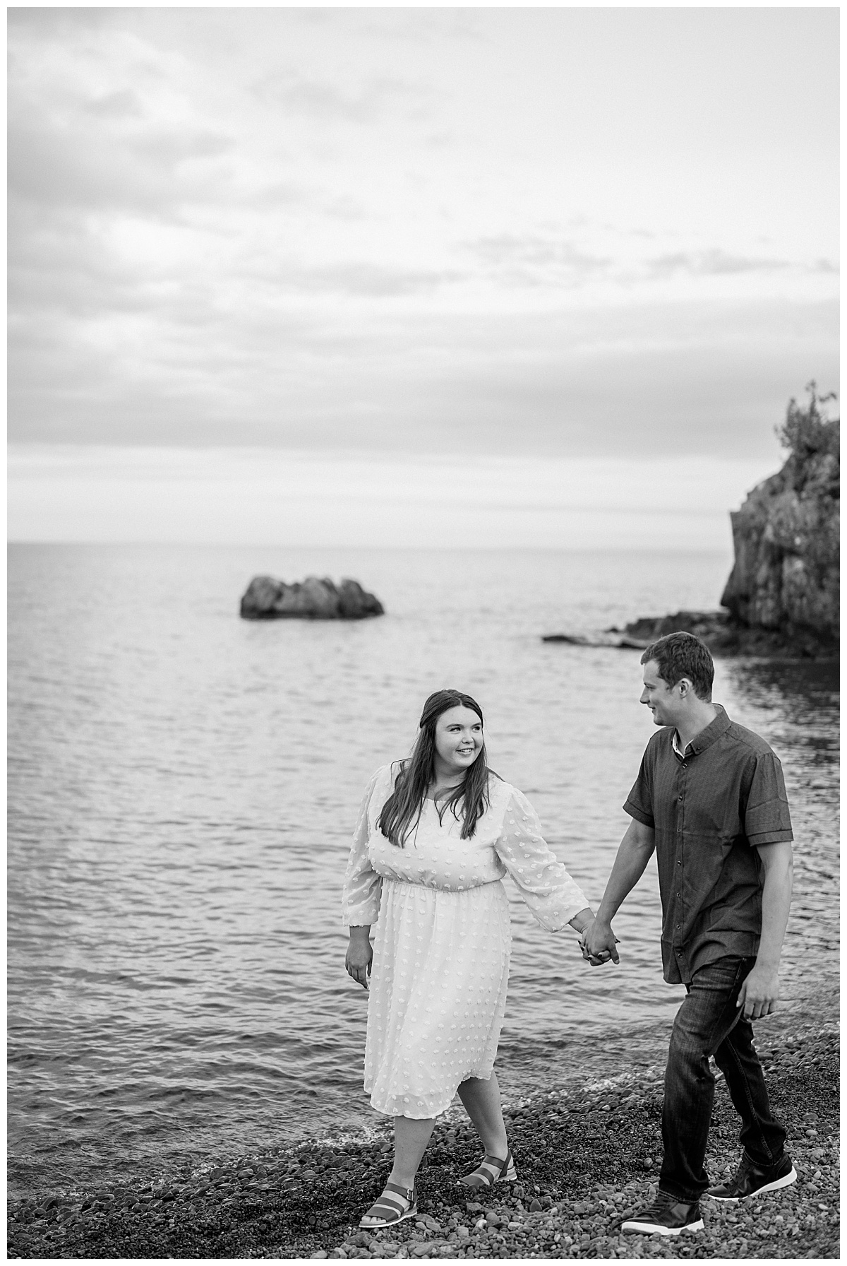 couple walks along shore holding hands and looking at each other by Minnesota wedding photographer