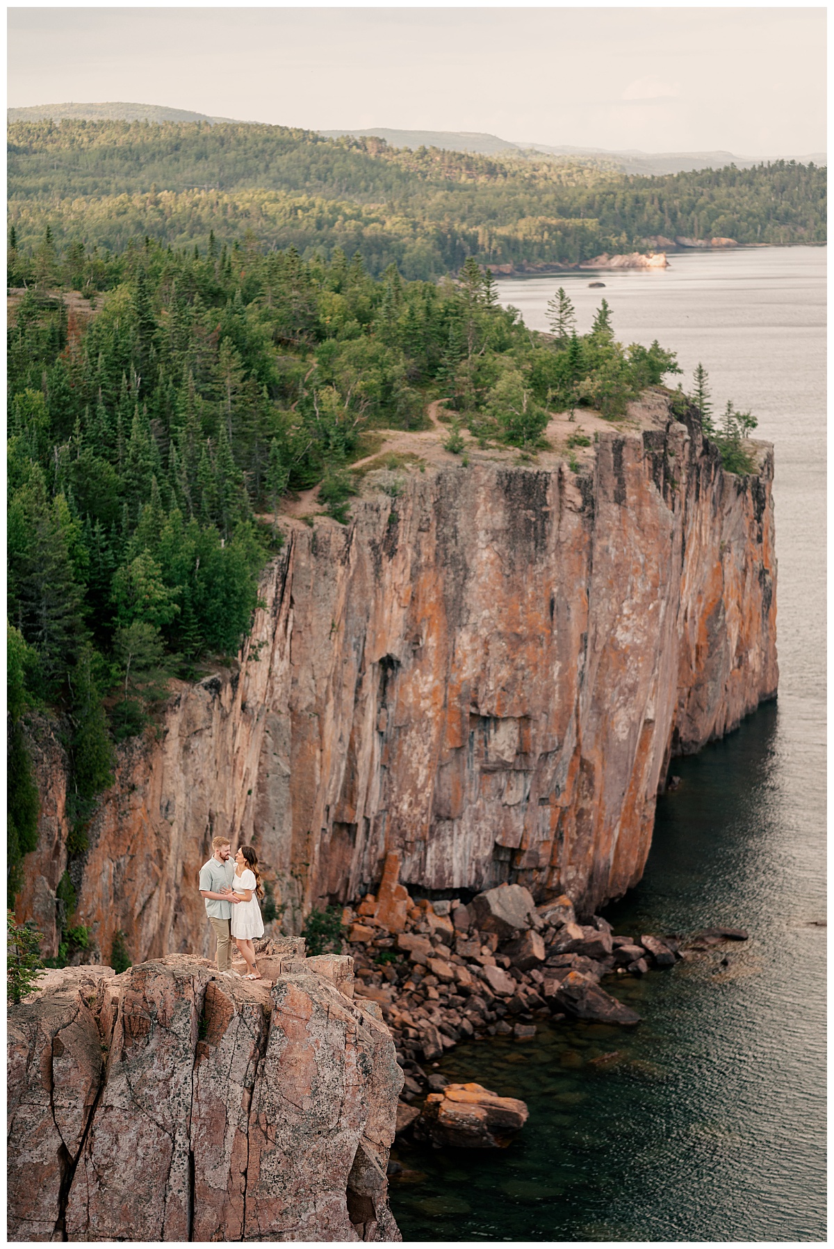 couple leans into each other standing on a cliff above water by Minnesota wedding photographer