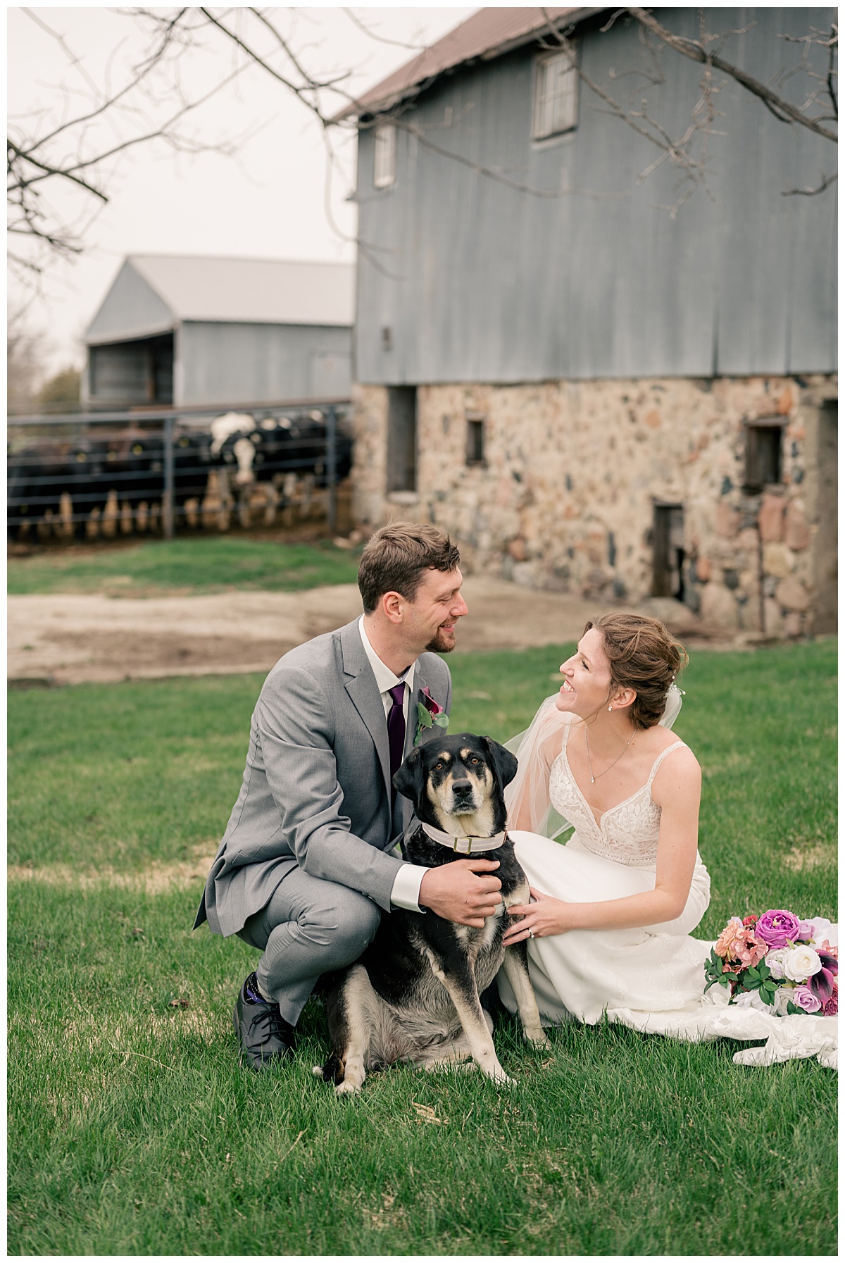 bride and groom smile at each other while holding their pup by Minnesota wedding photographer