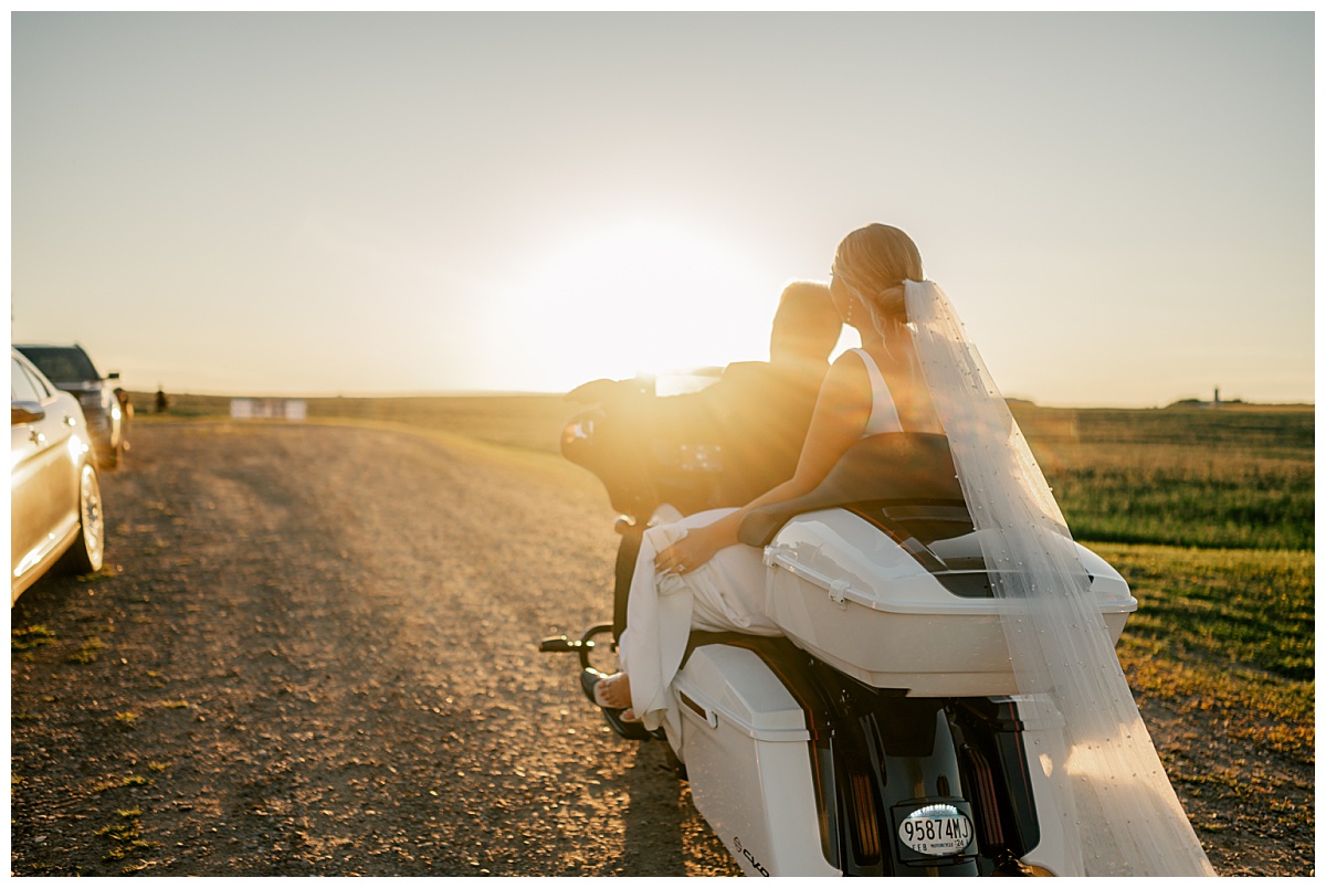husband and wife ride on motorcycle in wedding clothes toward the sunset by Minnesota wedding photographer 