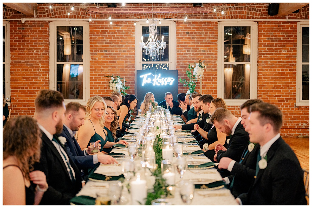bridal party and couple sit at long table at reception by Minnesota wedding photographer 
