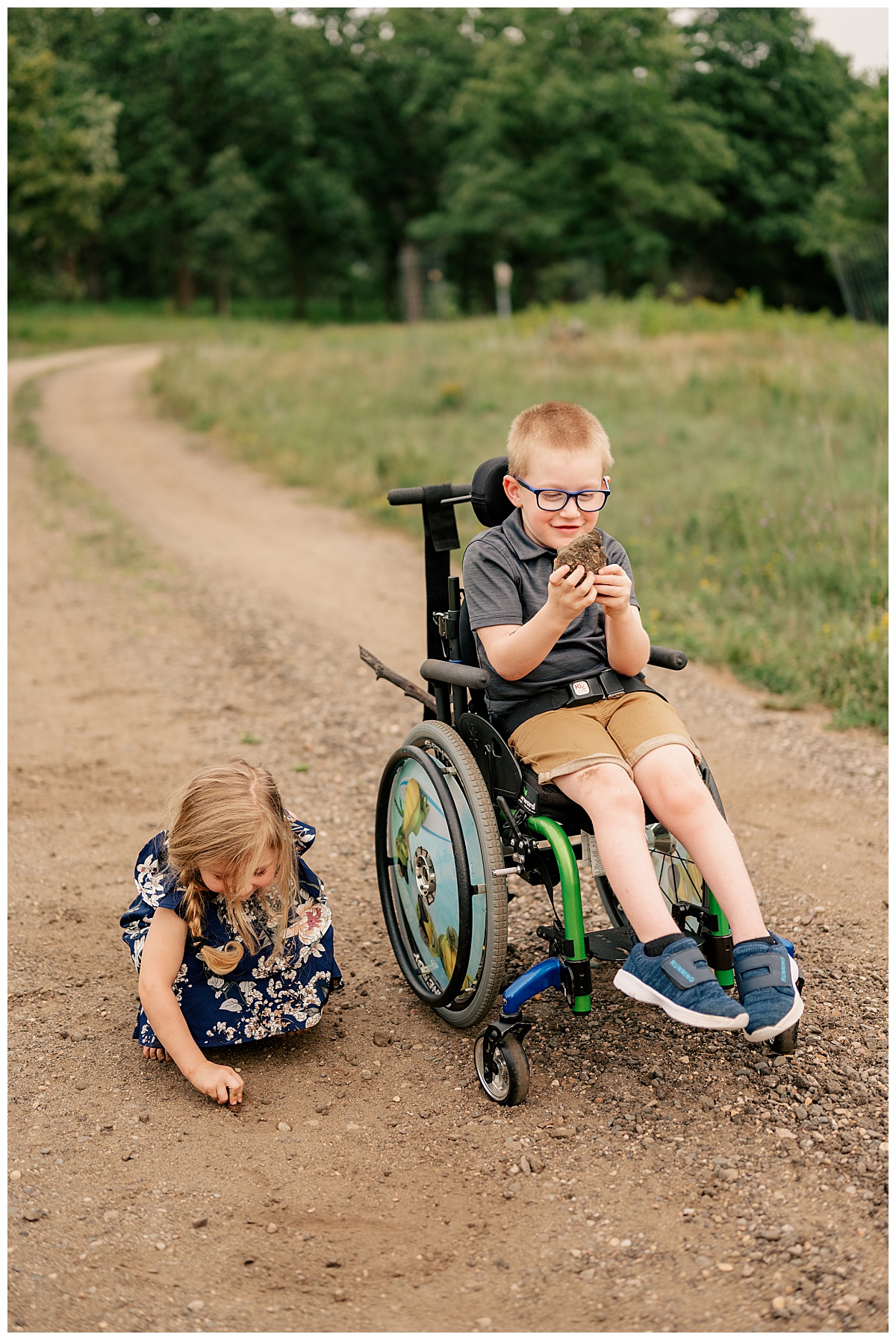 boy in wheelchair holds a rock as little girl draws in dirt during summer mini sessions