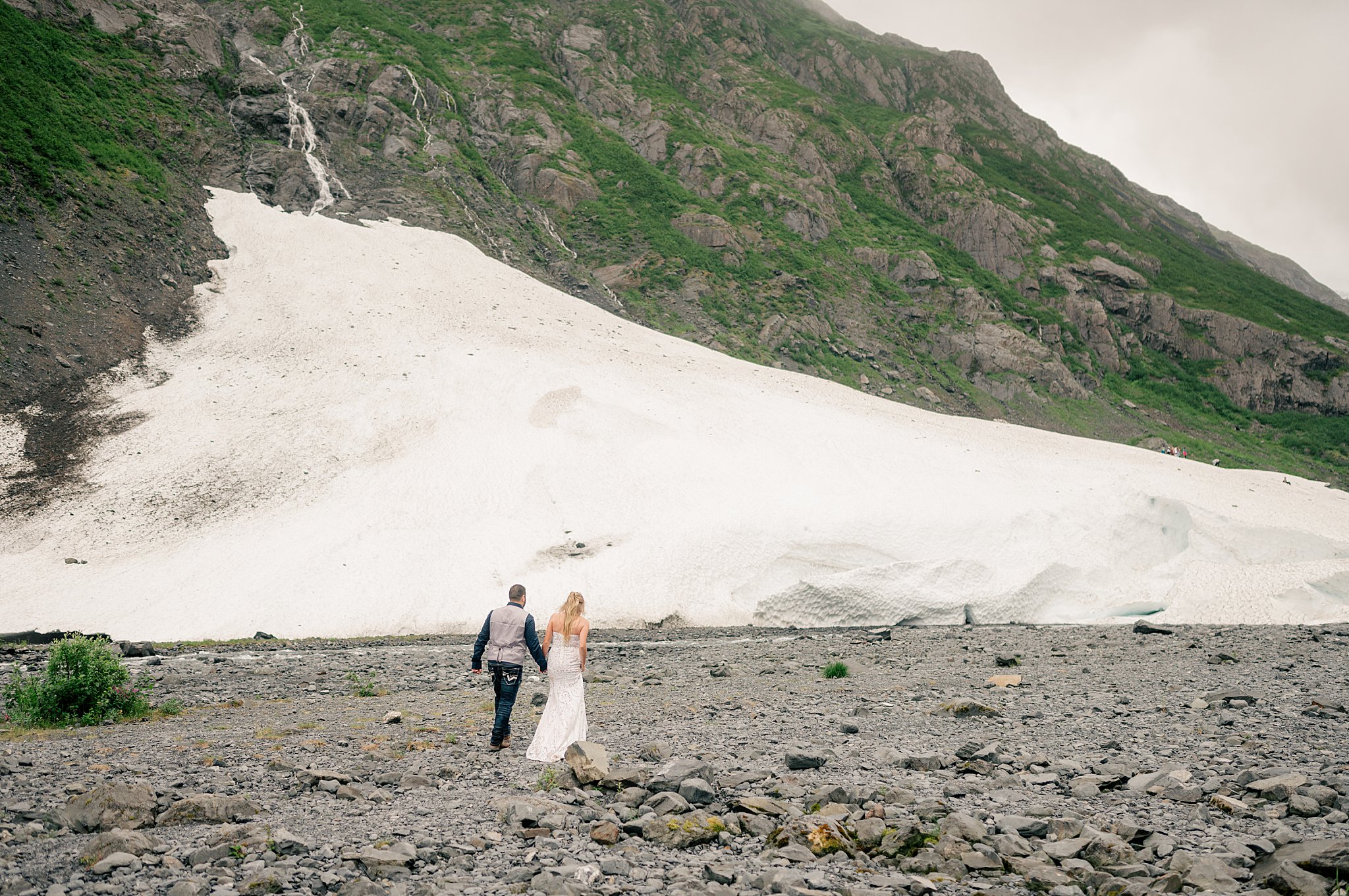 newlyweds hold hands as they walk in front of a glacier by Minnesota Wedding Photographer