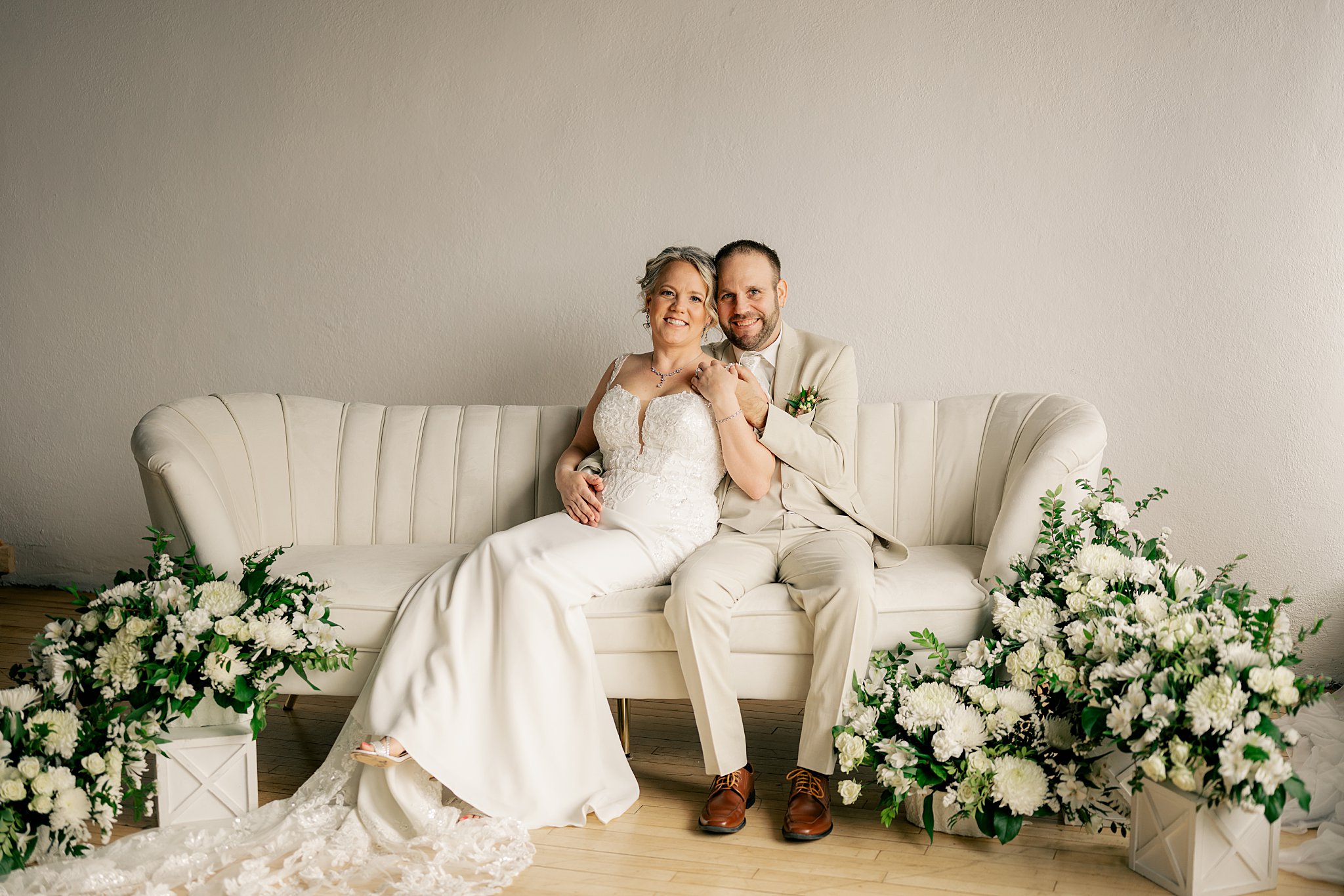 couple sits on couch in wedding attire surrounded by white florals by Rule Creative Co 