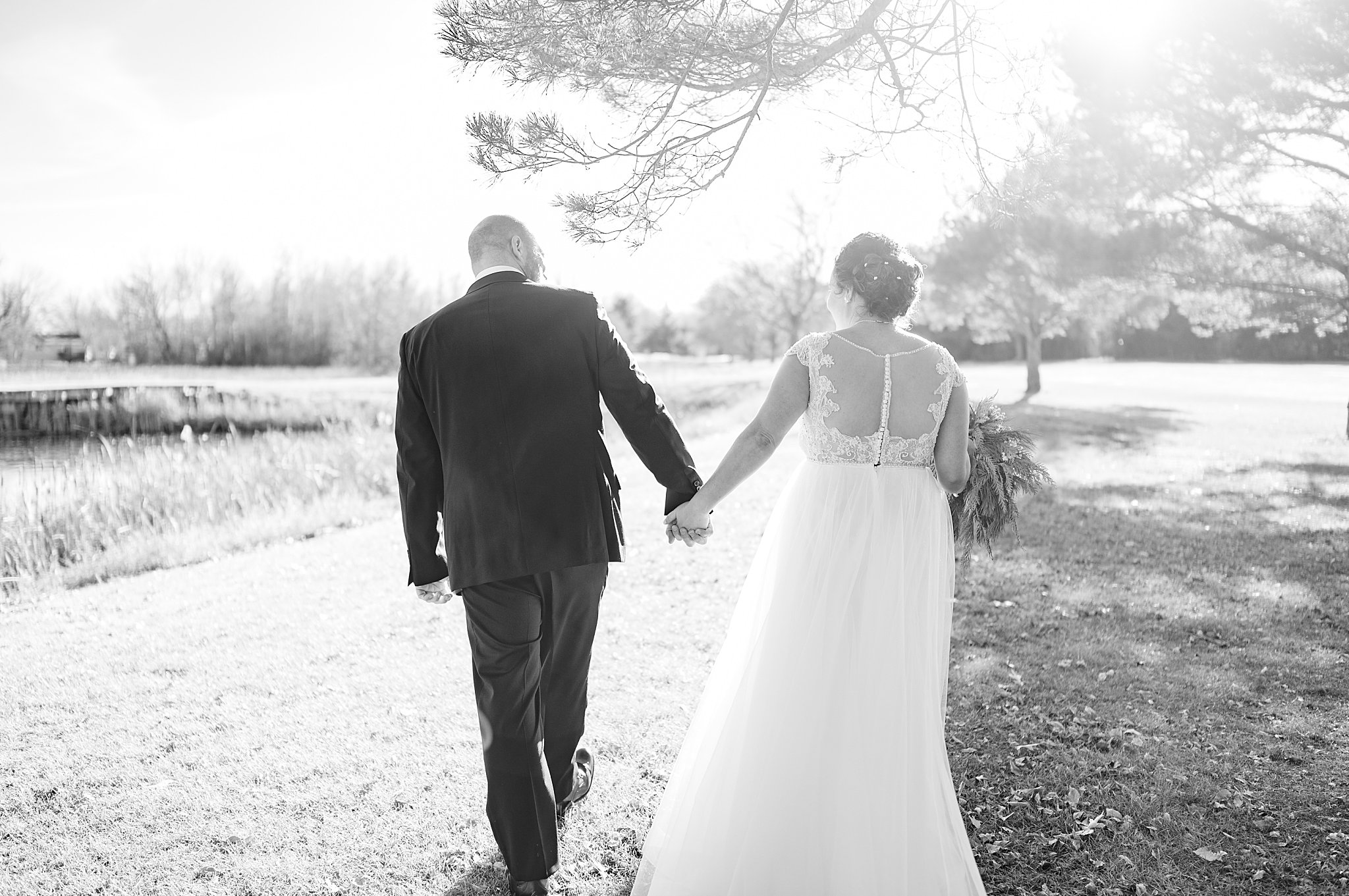husband and wife walk toward field hand in hand by Minnesota Wedding Photographer