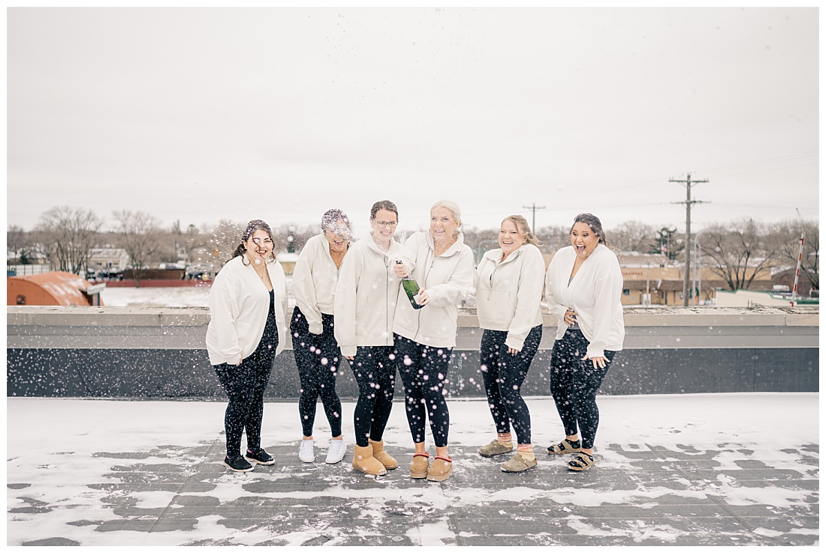 bridesmaids laugh as bride sprays champagne by Minnesota wedding photographer