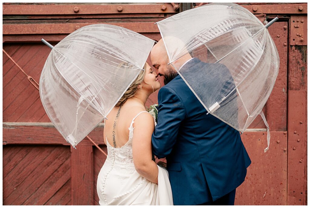 bride and groom touch noses under clear umbrellas as they embrace how to handle rain on your wedding day