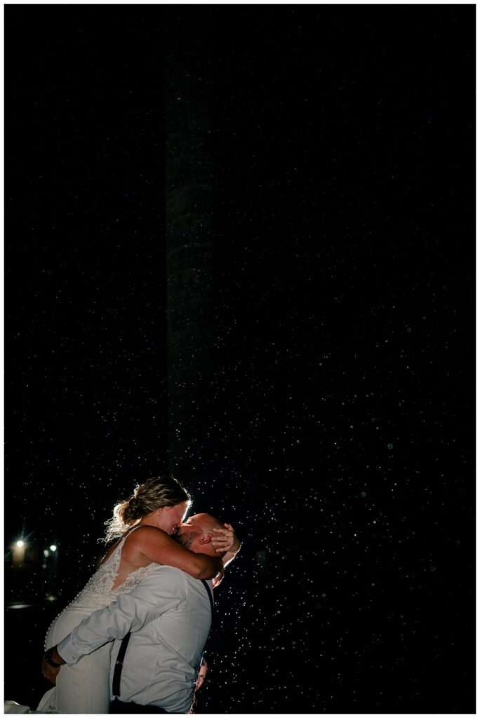 bride jumps into groom's arms as light shines from behind is one way how to handle rain on your wedding day