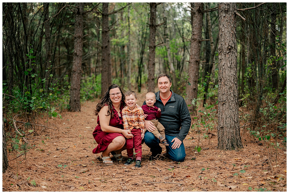 child smiles as he stands in the woods with family during fall mini sessions