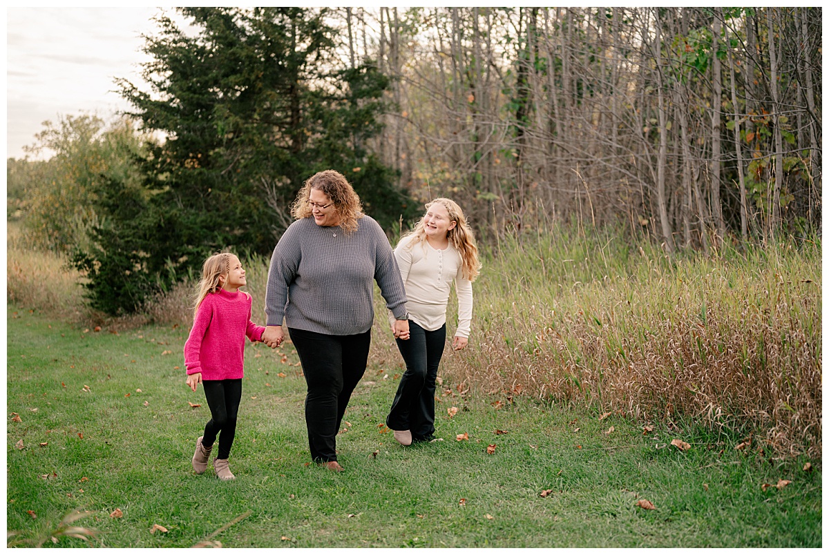 mom walks with daughters holding hands during fall mini sessions