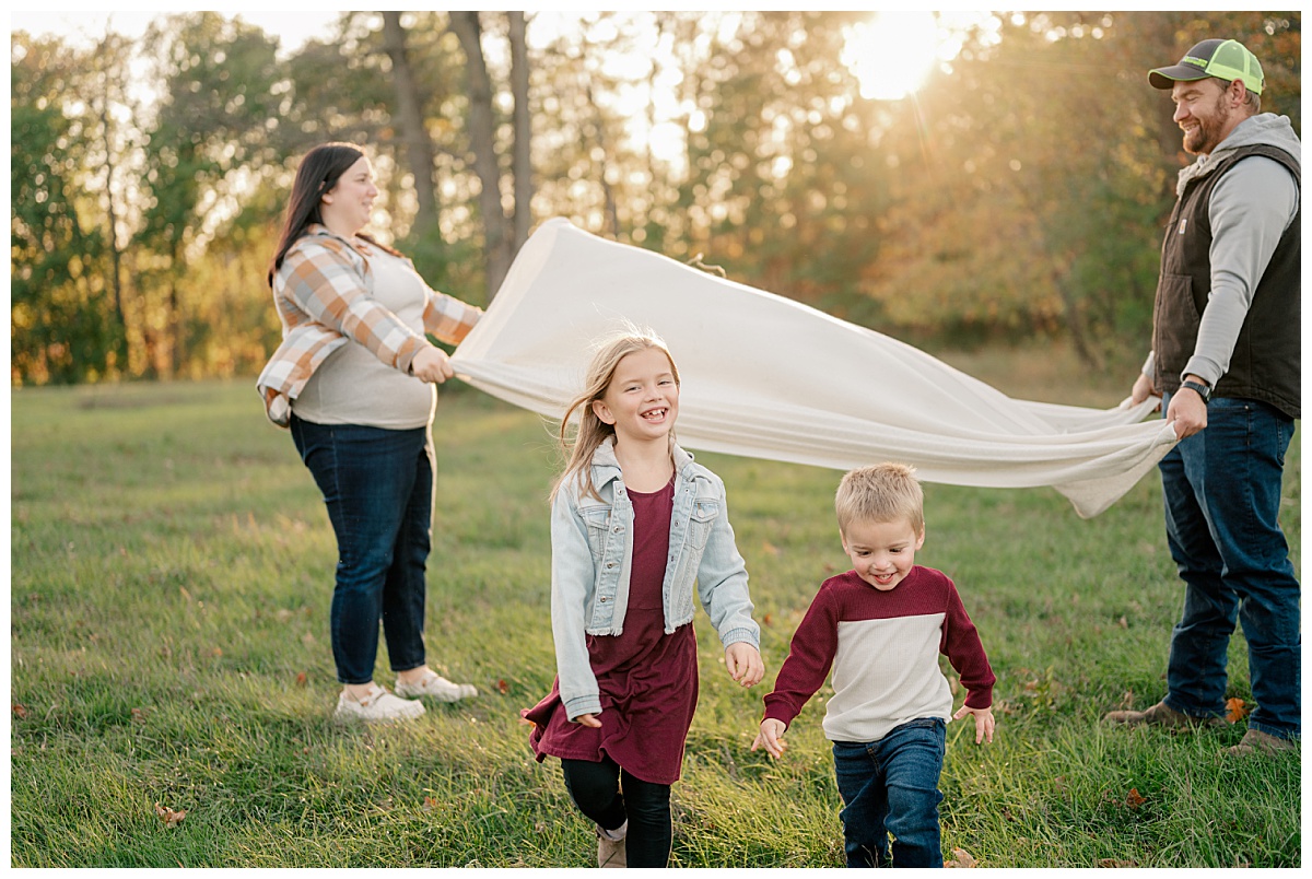 parents hold up blanket as kids run by Minnesota photographer