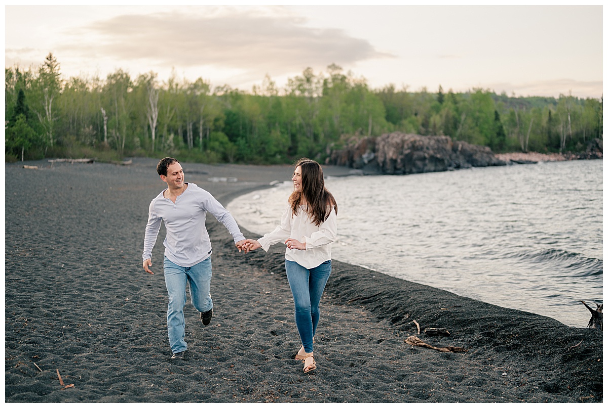 man and woman laugh and hold hands as they walk along shore by photographer sharing editing workflow