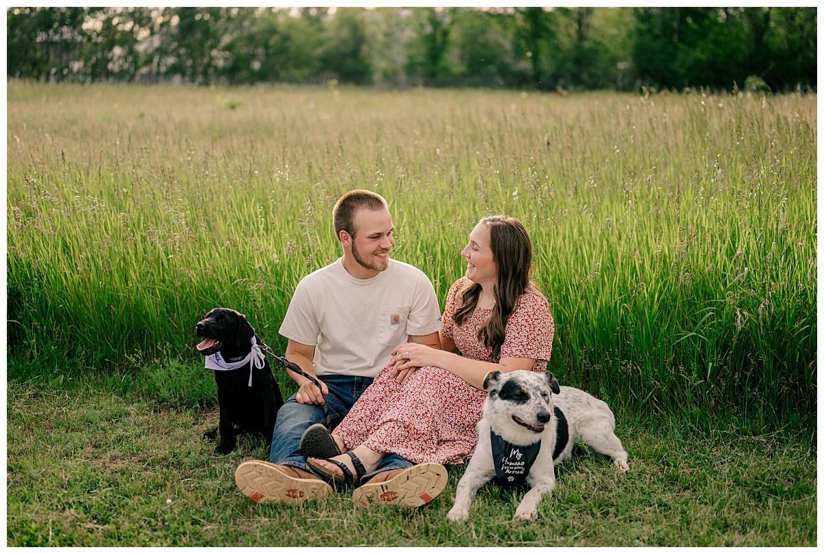 couple sits together on grass with their two dogs by Rule Creative Co