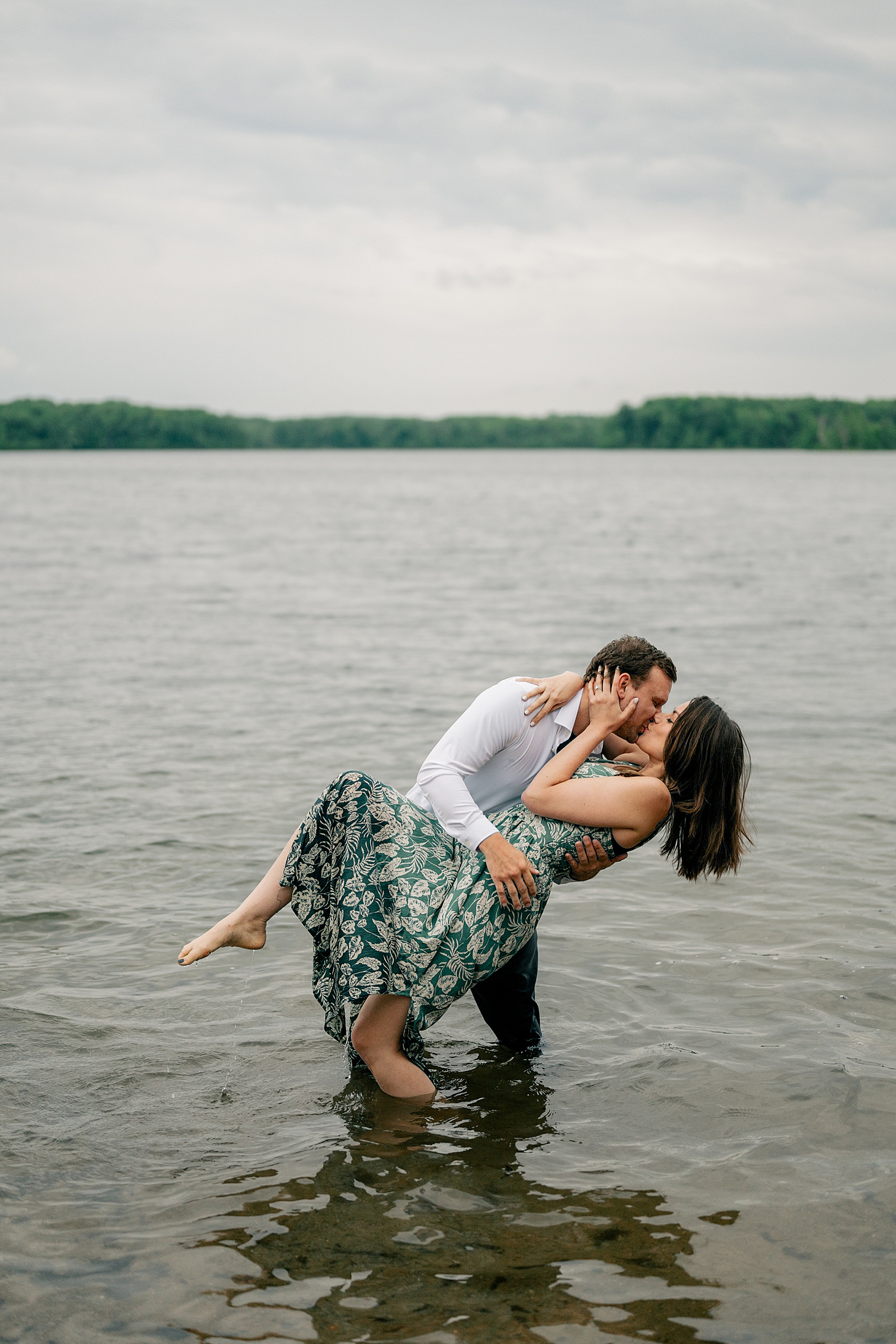 man dips his fiancé for a kiss in the lake by Minnesota wedding photographer