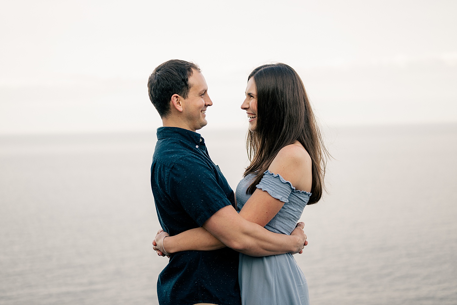 engaged couple embrace in front of the water for golden hour at North Shores