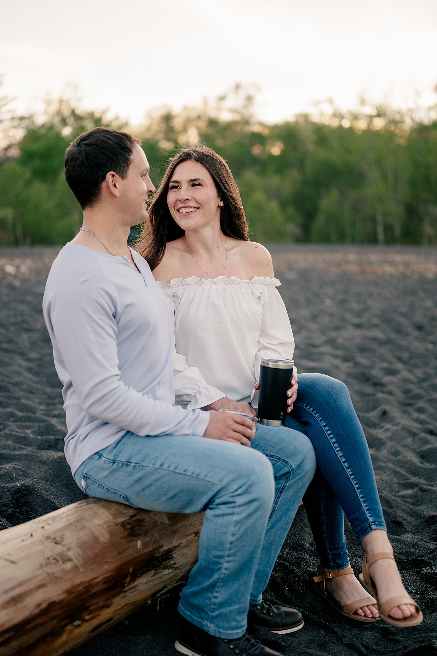 woman in white blouse and jeans snuggles her man on log by Minnesota wedding photographer