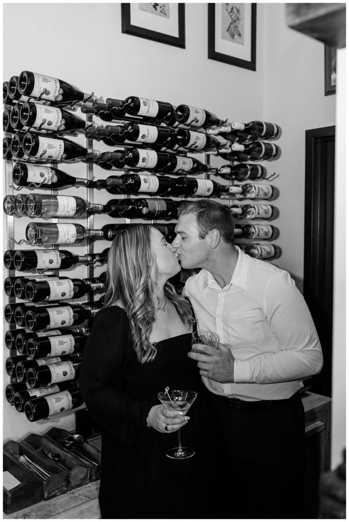 engaged couple kisses in front of wine bottles by Rule Creative Co