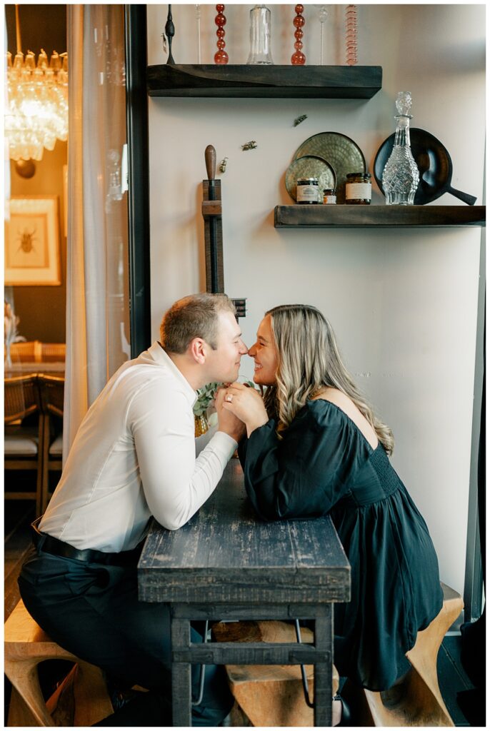 engaged couple leans across table to touch noses by Minnesota wedding photographer