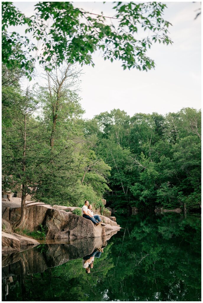 engaged couple sits on rocks overlooking lake by Rule Creative Co