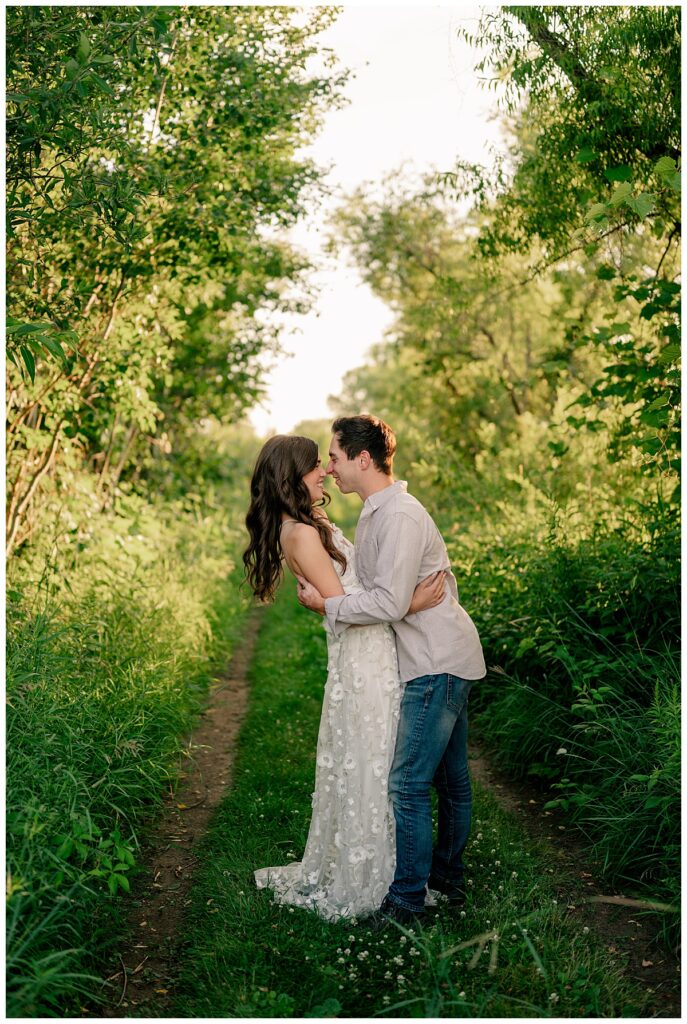 engaged couple leans in for a kiss on a wooded path by Rule Creative Co