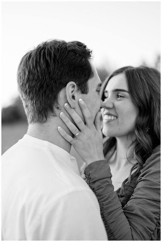 woman places hand on man's face while she leans close at golden hour St. John's engagement 