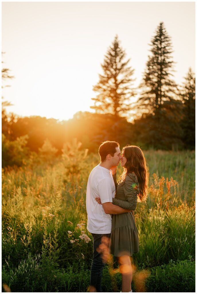 couple leans in for a kiss as sun glows behind them at golden hour St. John's engagement 