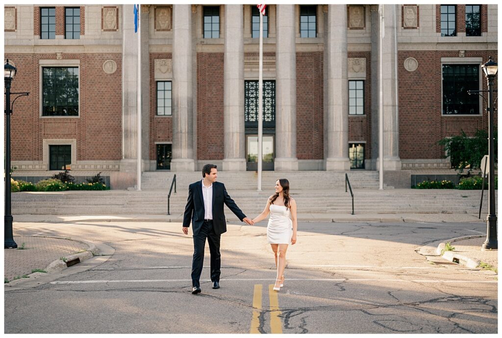 couple crosses street holding hands at My Favorite Central Minnesota Engagement Session Locations