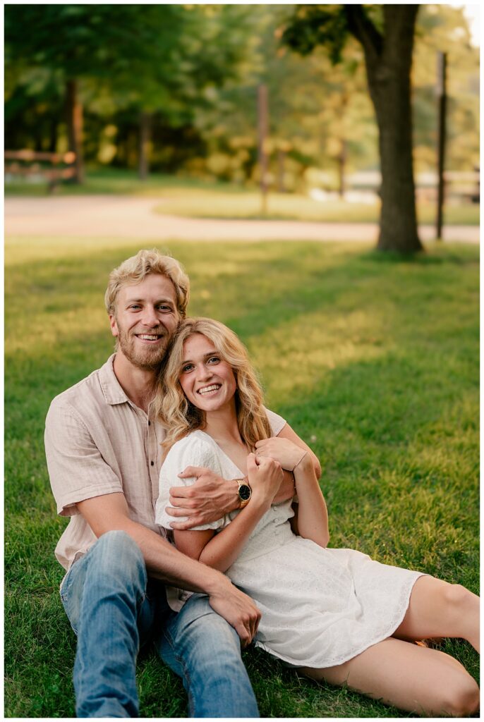 woman leans against fiance on lawn by Minnesota wedding photographer