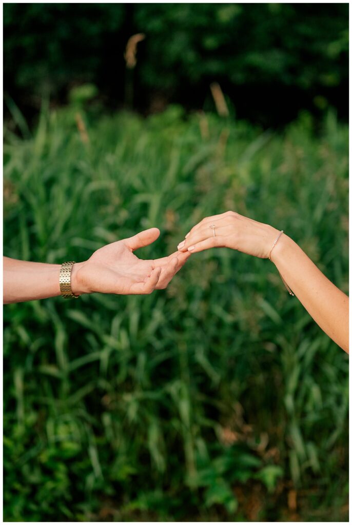 woman places hand in man's outstretched hand at Fish Park engagement session