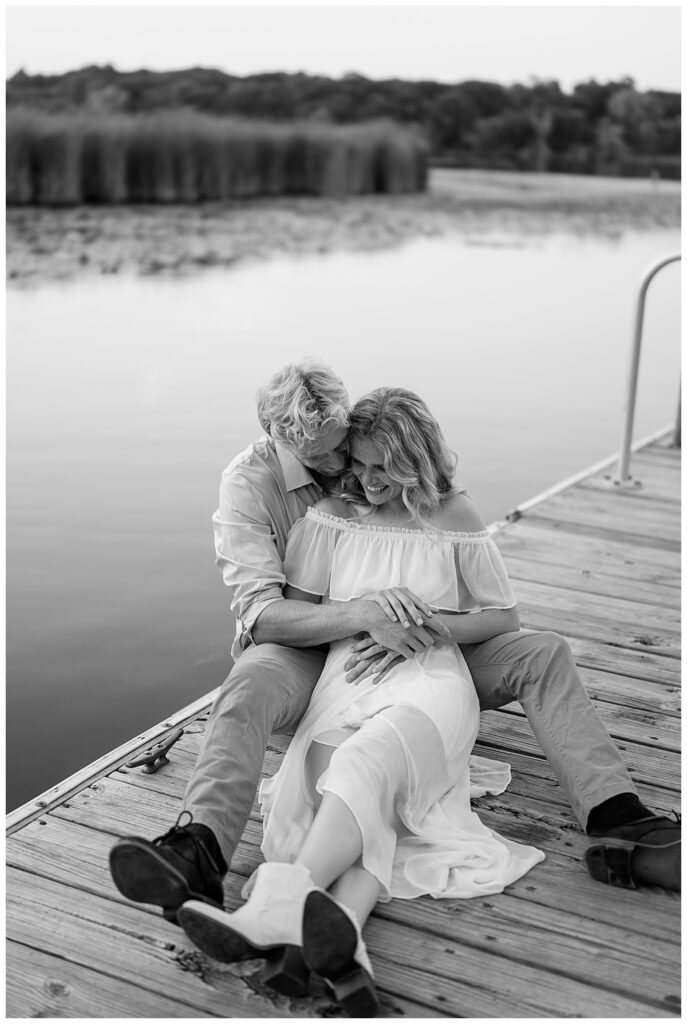 man and woman sit together smiling on dock at Fish Park engagement session