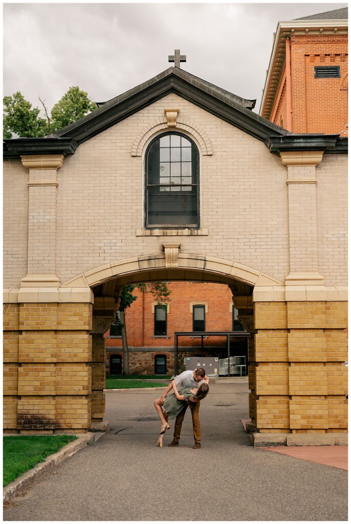 man dips woman and kisses her under archway by engagement at St. John's University