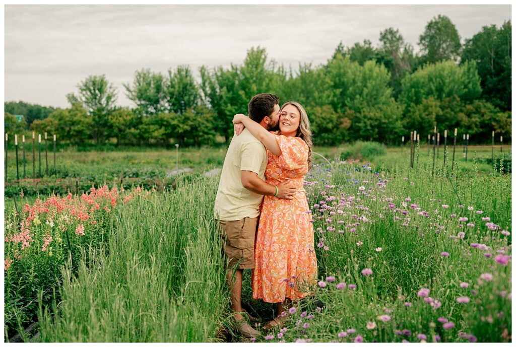 man kisses wife on cheek at flower farm couples session