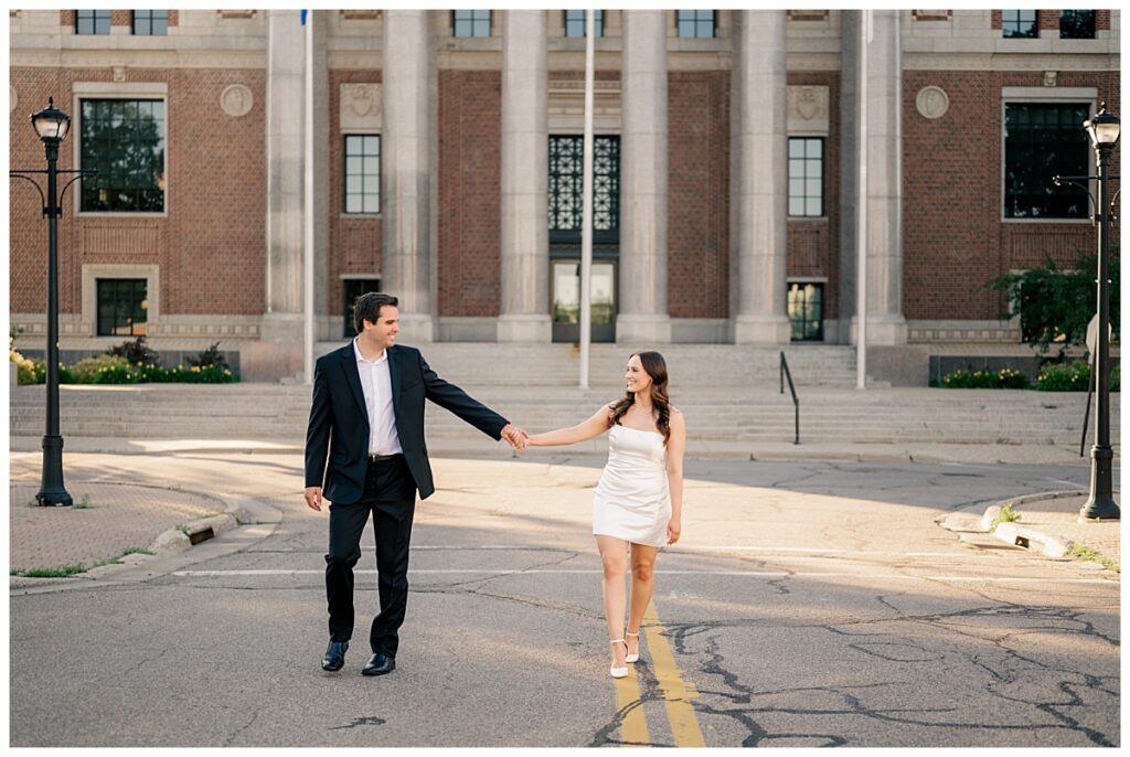 couple walks in middle of road holding hands at Downtown St. Cloud engagement session