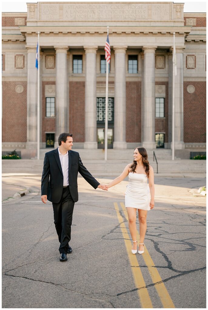 couple holds hands smiling at each other as they walk down the street by Minnesota wedding photographer