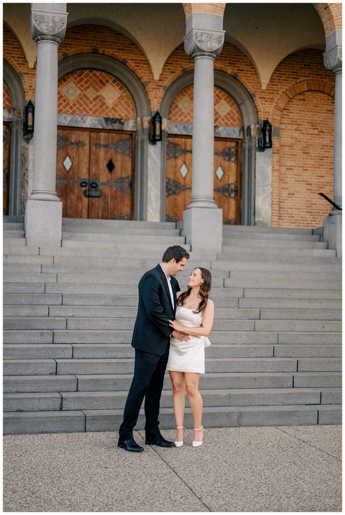 couple looks at each other smiling in front of ornate building at Downtown St. Cloud engagement session