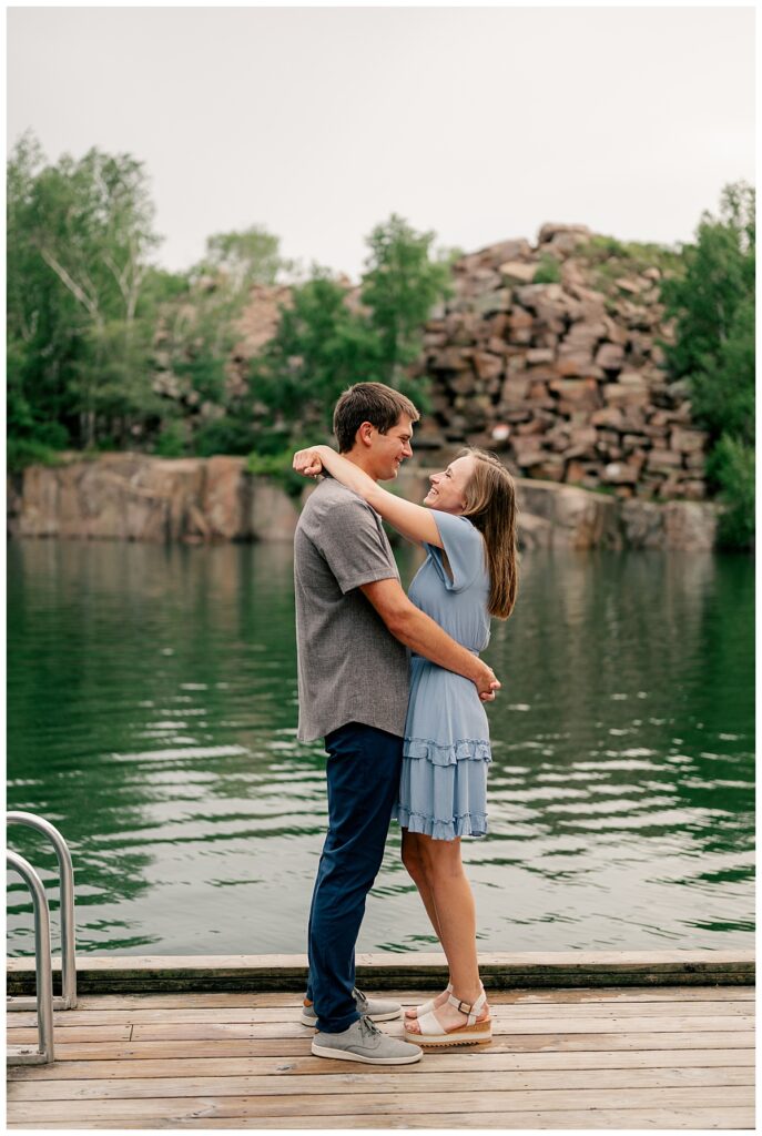 man and woman wrap arms around each other in front of reflecting lake at Nature Preserve engagement session