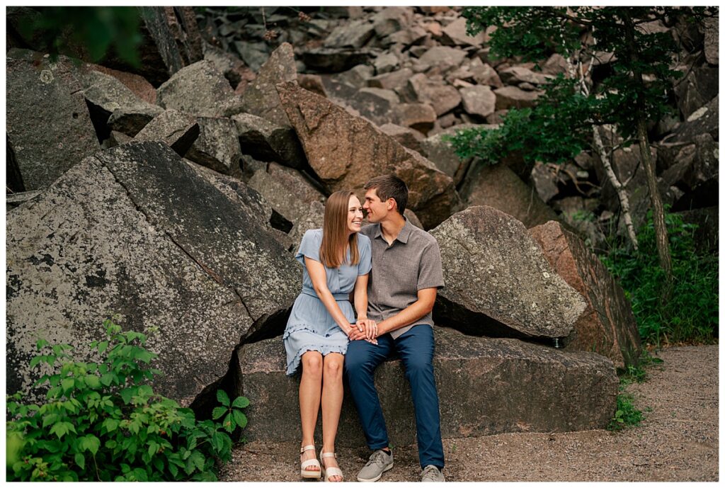 engaged couple sit together on a large rock by Minnesota wedding photographer