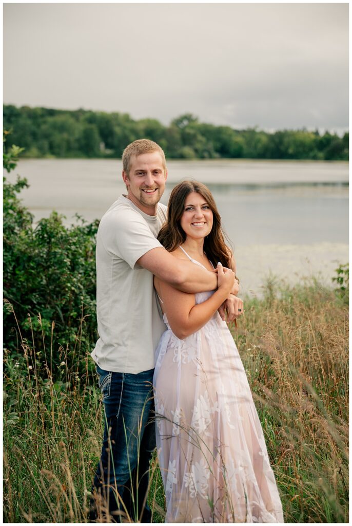 husband wraps arms around wife's shoulders as they smile by Minnesota couples photographer