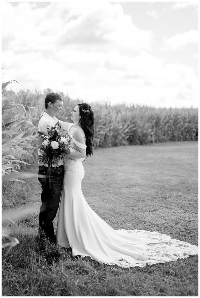 bride and groom put arms around each other near corn field by Rule Creative Co