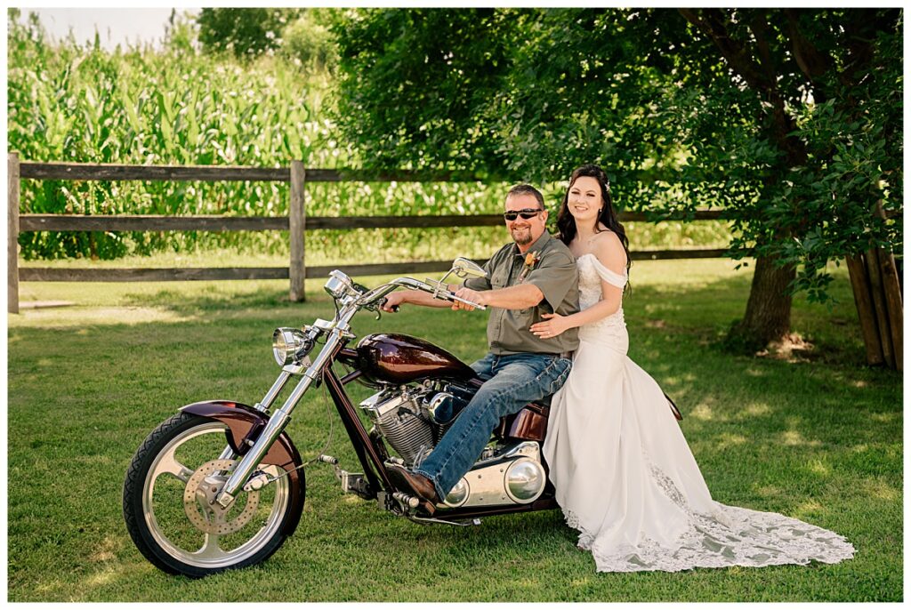 woman sits on back of her dad's motorcycle in a gown at late summer Central Minnesota wedding