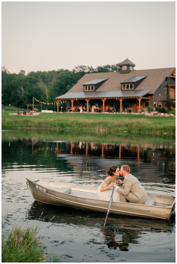 couple kisses in boat on pond in front of barn by Minnesota wedding photographer