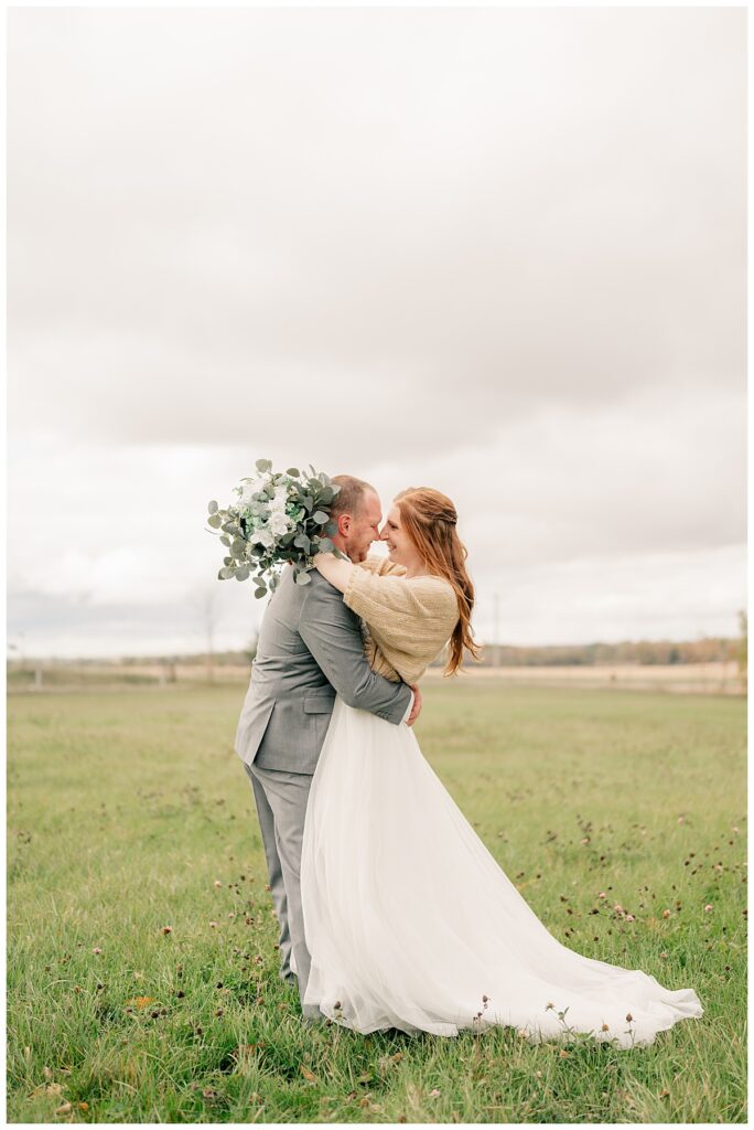 bride and groom wrap arms around each other in meadow by Rule Creative Co