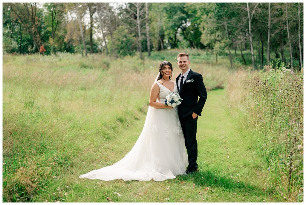 man and woman stand together in meadow at late summer wedding in Paynesville