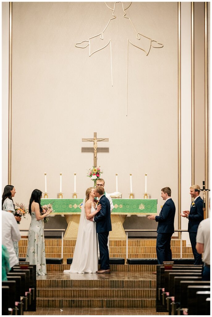 man and woman kiss during the ceremony at their Northern Oaks summer wedding