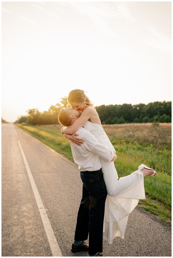 groom picks up bride and kisses her as sun sets by Rule Creative Co