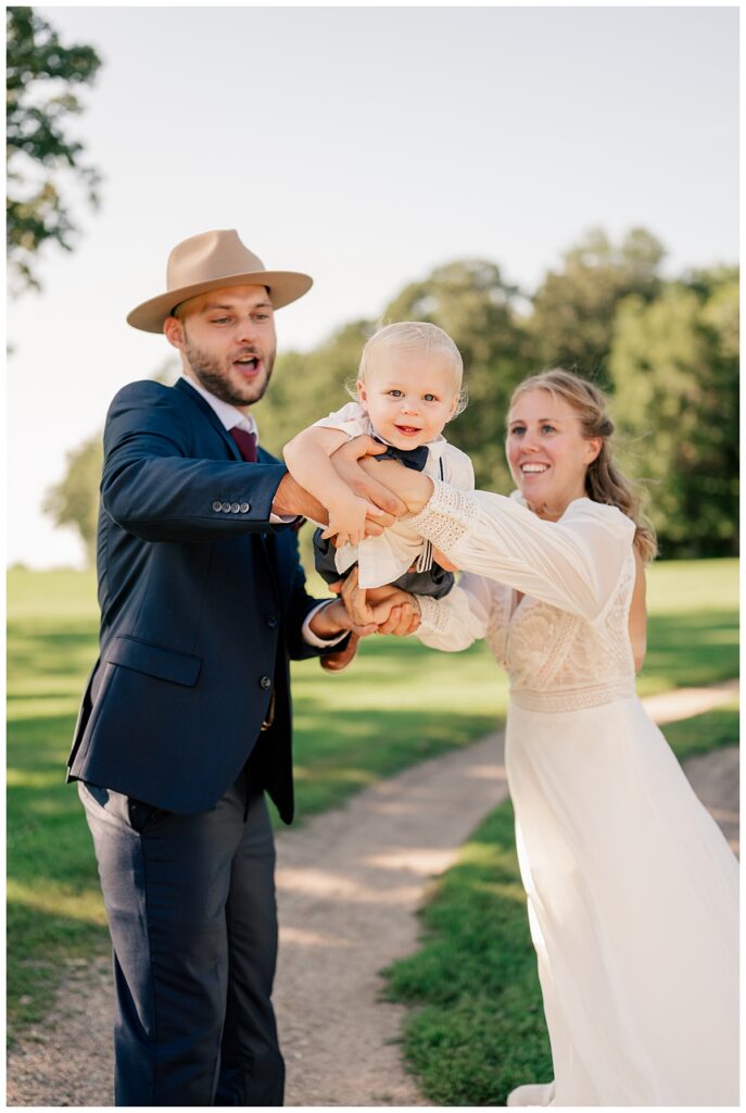 parents swing young child as he smiles by Minnesota wedding photographer