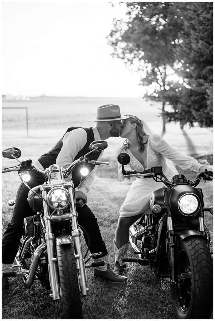 man and woman on motorcycles lean in for a kiss after intimate outdoor summer wedding