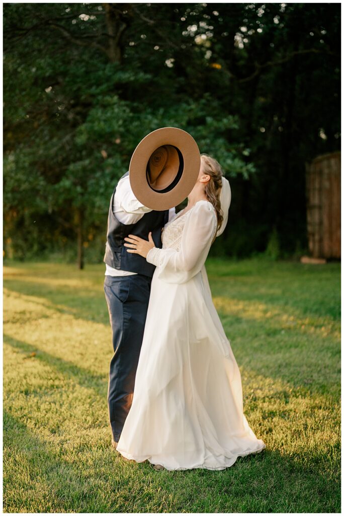 man holds out hat to cover faces as he kisses woman by Minnesota wedding photographer