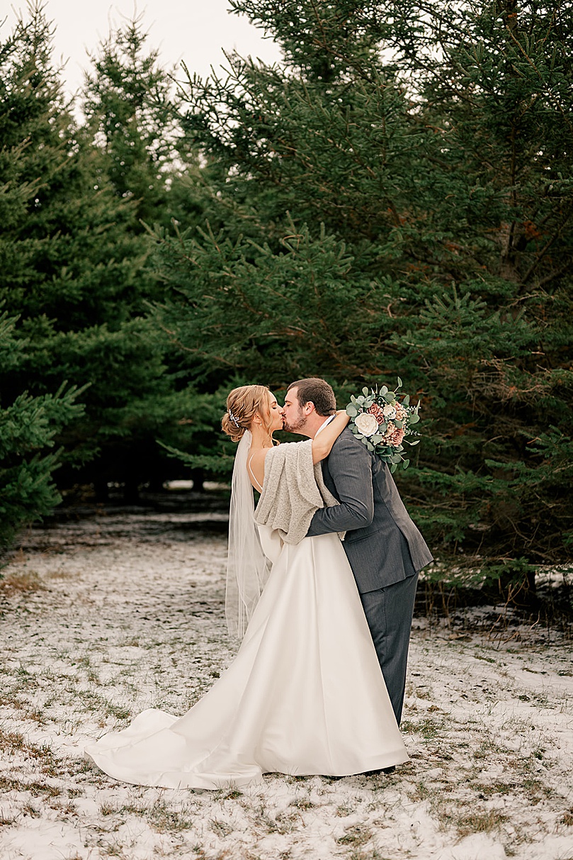 groom leans in to kiss bride in snow for Romantic Winter Wedding in Brooten